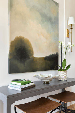 A minimally styled console table with leather ottomans below and landscape oil painting above